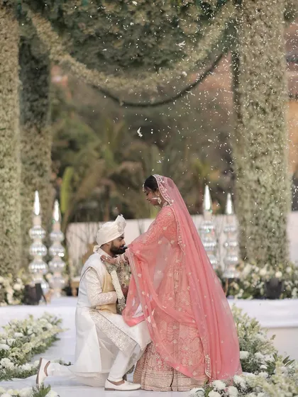 A tender moment during the varmala ceremony. The groom, on one knee, kisses his bride's hand under a shower of petals, a gesture of love and respect that I helped stage against a beautiful floral backdrop.