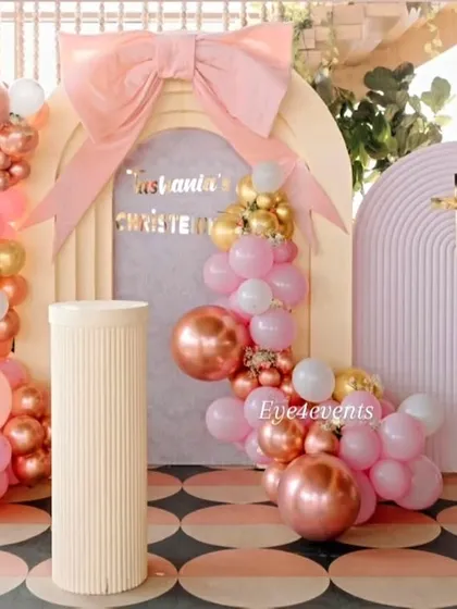 We design elegant and modern christening celebrations. This setup features a beautiful backdrop of arched panels in pastel purple, accented with a large pink bow and balloon arrangements in shades of pink, white, and rose gold for a truly special day.