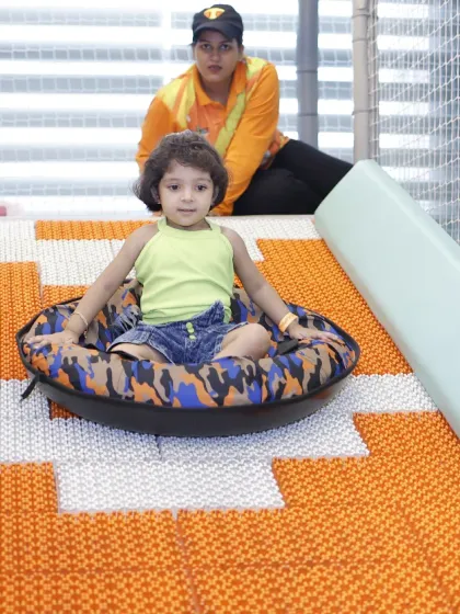 A young child sits in a tube at the top of the Donut Slide, ready for an exciting ride down with our staff member nearby.