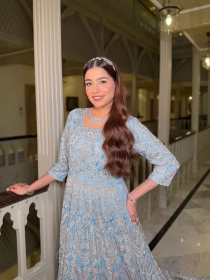 A full view of the magnificent blue gown. The makeup is kept soft and romantic, with a focus on glowing skin and a gentle pink lip to complement the cool tones of the dress.