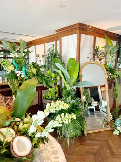 A lush, tropical-themed decor for a collection launch, featuring large banana leaves, coconuts, and a rattan mirror.