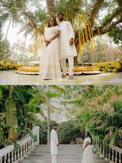 A couple stands together in pristine white outfits against a backdrop of lush greenery and yellow marigolds, creating a beautiful contrast.
