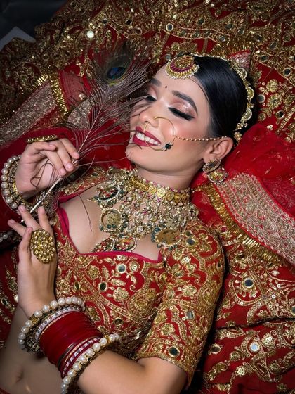 A beautiful candid of a bride lying down, surrounded by her rich red lehenga. Her makeup is flawless, with a focus on glowing skin and a happy smile.