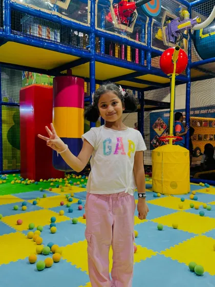 A girl flashes a peace sign in the middle of the ball pit area, surrounded by colorful balls and play structures.