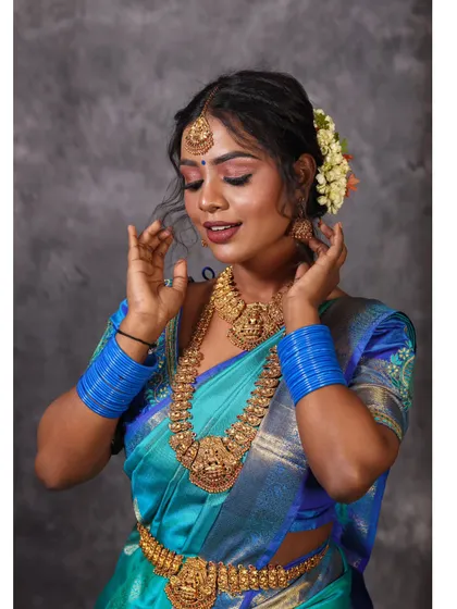 A serene portrait of a model in a blue silk saree, adorned with traditional jewelry. The soft lighting and gentle pose create a timeless and elegant feel.