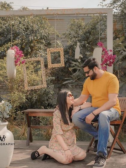 A sweet and tender moment from a garden pre-wedding shoot, with the groom affectionately touching the bride's face as she sits at his feet.