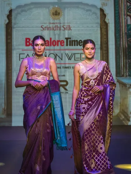 Two models showcasing a collection of silk sarees on the ramp. This image is useful for lookbooks and event coverage, as it displays multiple pieces from a designer's line.