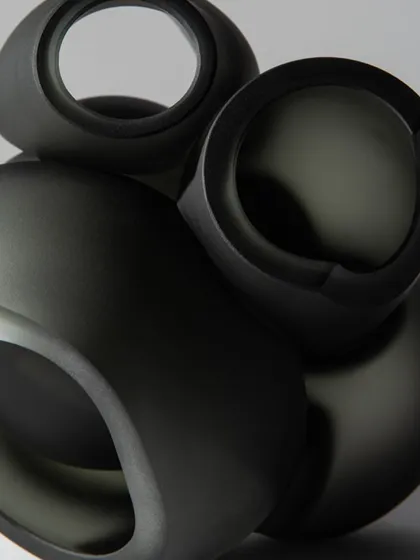 A detailed shot of the matte, dark grey finish of the Bocci 100 series pendants, highlighting their smooth, sculptural quality.