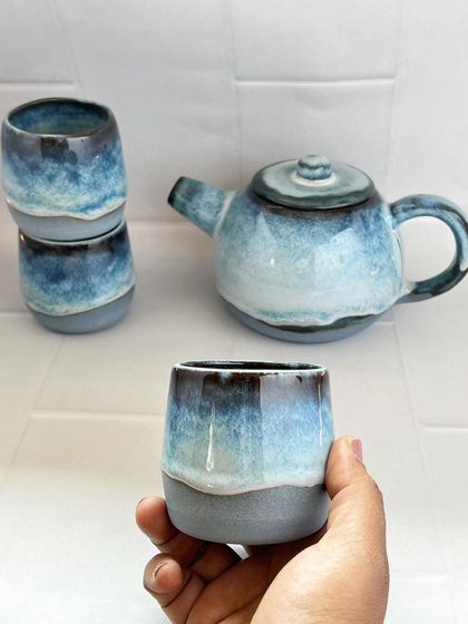 Holding one of the small tea cups from the set. They are designed without handles, in a traditional style, to be warmed by the tea and cupped in your hands.