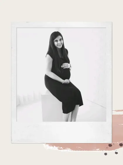 A simple and classic black and white portrait. The seated mother-to-be smiles warmly, creating a timeless and joyful image in a polaroid-style frame.