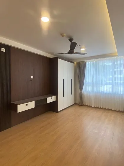 This master bedroom is designed as a personal retreat, featuring a custom-built TV unit and wardrobe, warm wooden flooring, and elegant lighting to create a serene atmosphere.