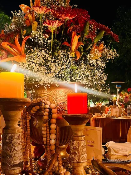 A close-up of the table setting for the Sunderkand event. The decor features warm, earthy tones with orange and red candles and traditional beaded elements.