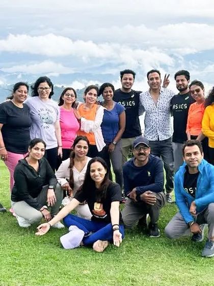 A group photo on a lush green hilltop in Nepal, with clouds below us. Together, we reach new heights.