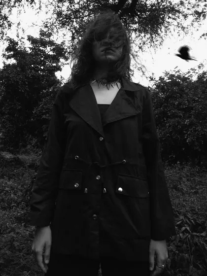 A chaotic and moody black and white portrait shot outdoors. The wind-blown hair obscuring the face and the bird in flight create a sense of beautiful disarray.