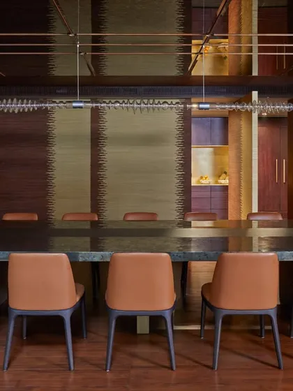 A full view of the Baid Residence dining room, showcasing the long table, leather chairs, and the unique light fixture. The room is paneled in wood, creating a warm and intimate atmosphere for gatherings.