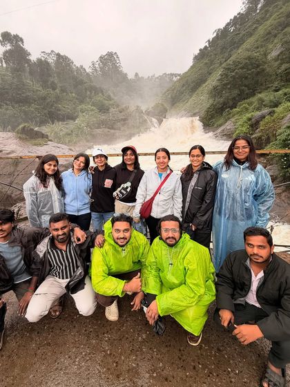 Our group posing in their raincoats in front of a powerful waterfall in Munnar.