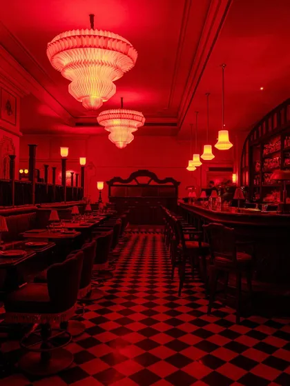 The interior of BANNG in Gurgaon is saturated in a bold, monolithic red, creating an electrifying and immersive atmosphere. This view down the main axis showcases the interplay of the checkerboard floor, custom chandeliers, and deep-set booths, crafting a vibrant narrative of Thai-Indian fusion.