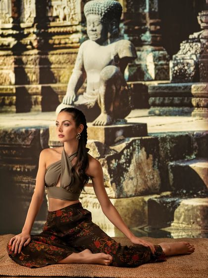 A serene temple backdrop is projected to create a peaceful, spiritual mood. The lighting is soft and warm, complementing the model's meditative pose and the cultural setting.