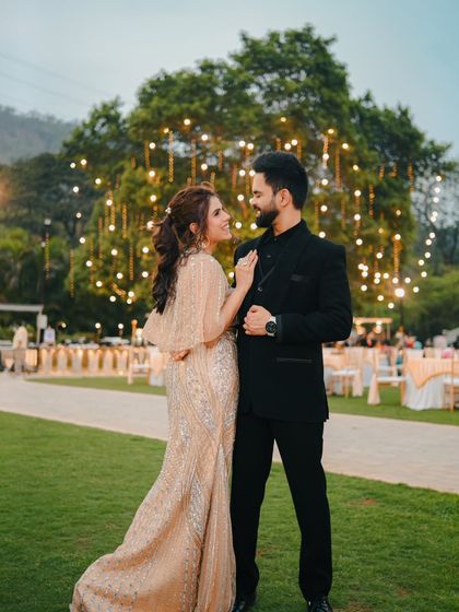 A classic portrait of a couple in elegant evening wear, set against a beautifully lit outdoor venue. This photo captures a sense of glamour and celebration.