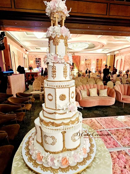 Another perspective of the grand architectural cake, showcasing its intricate details against the backdrop of the elegant event space. The lighting highlights the gold accents and the texture of the sugar work.