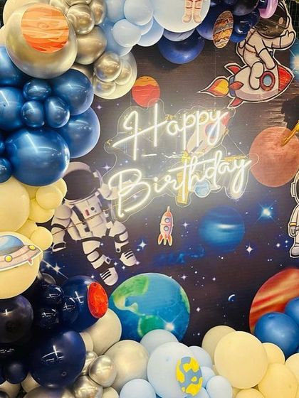 A close-up of the space-themed balloon arch, showing detailed planet balloons, astronaut cutouts, and a 'Happy Birthday' neon sign against a galaxy backdrop.