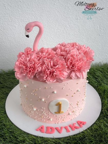 A flamingo-themed cake for a first birthday, adorned with beautiful fresh pink carnations. The soft pink frosting and gold accents create a sweet and stylish look.