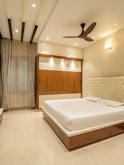 A serene bedroom with a tufted cream headboard, complemented by wood paneling and soft, ambient lighting.