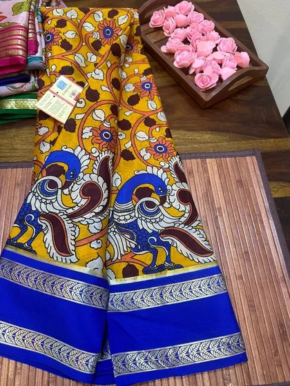 A traditional peacock motif Kalamkari print on a yellow Mysore silk saree with a blue border.
