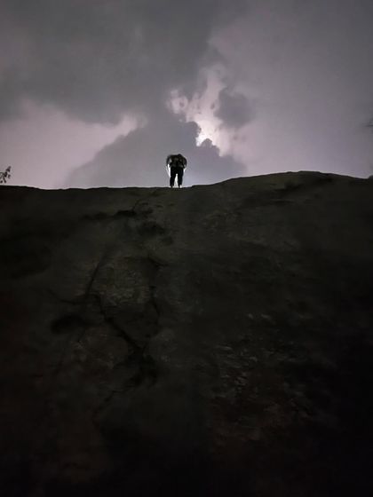 A climber stands silhouetted against a dramatic sky filled with lightning. While we always prioritize safety, sometimes nature puts on a spectacular show for us.
