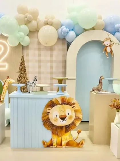 A soft and modern take on a jungle theme for a second birthday. The decor uses a pastel blue and beige color palette with cute, cartoonish animal props like a lion, giraffe, and zebra.