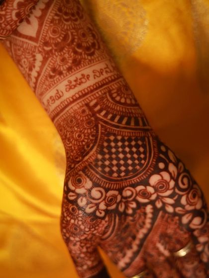A close-up of a bride's arm with her and her partner's names beautifully written in Kannada script, nestled within the traditional design.