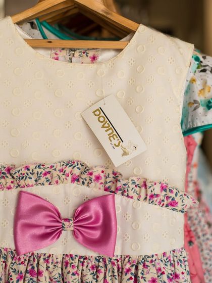 A close-up of a dress in my studio, highlighting the combination of a textured white bodice and a floral ruffled waistline, all tied together with a bold pink bow.