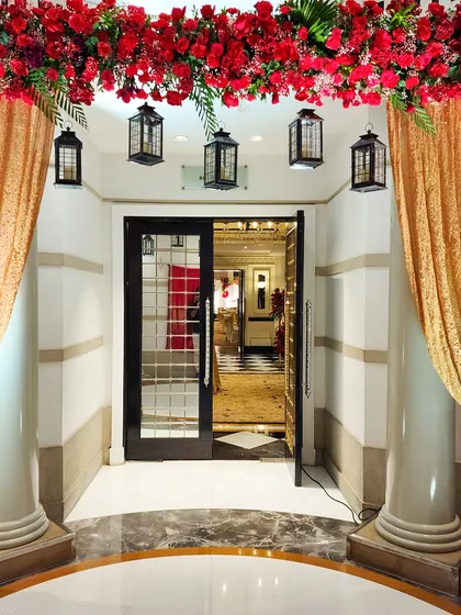 A simple yet elegant entranceway featuring golden drapes, hanging lanterns, and an overhead garland of red flowers. This design adds a touch of warmth and traditional charm to the venue's doorway.