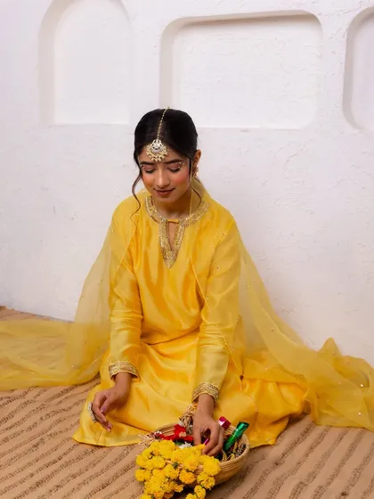 A seated pose in the yellow suit, creating a serene and graceful moment. The delicate organza dupatta adds a touch of softness to the look.