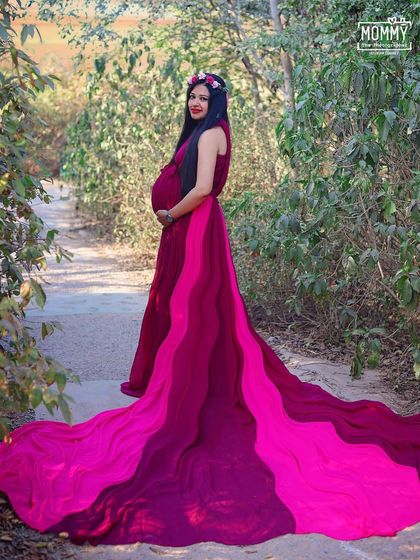 Feeling like a queen of the forest. This mom-to-be is stunning in a vibrant magenta gown, with the long train spread out behind her in this enchanting outdoor maternity portrait.