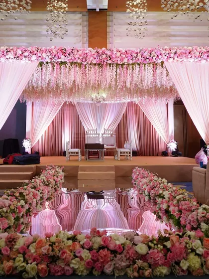 A fairytale reception stage with a mirrored aisle reflecting the canopy of pink flowers and cascading wisteria. The soft pink drapes and lighting create a dreamy, romantic ambiance.