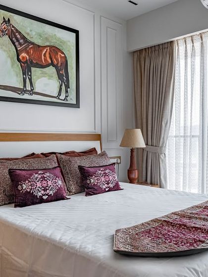 The 'Eternity' guest bedroom, featuring a prominent piece of equestrian art above the bed. The color palette is warm and neutral, with pops of deep red in the cushions and runner.