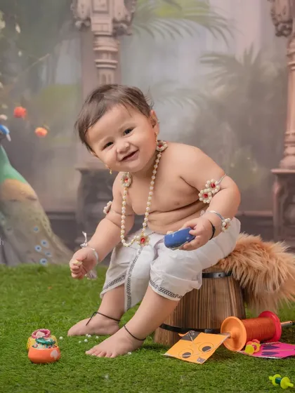 A unique blend of themes, this happy baby is dressed in a simple traditional outfit for Makar Sankranti, with kites and string at his feet, set against a beautiful palace backdrop.