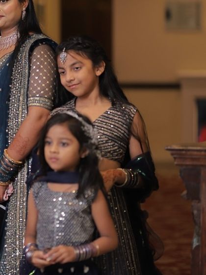 Two young sisters in coordinated custom outfits. One wears a navy sequin lehenga while the younger one is in a matching silver top.