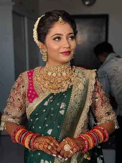 A beautiful bride in a green Paithani saree with a pink border, adorned with heavy gold jewellery.