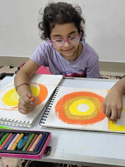 Two students collaborate on an oil pastel drawing. Working together on a single piece of art teaches them communication, teamwork, and how to blend different creative ideas.