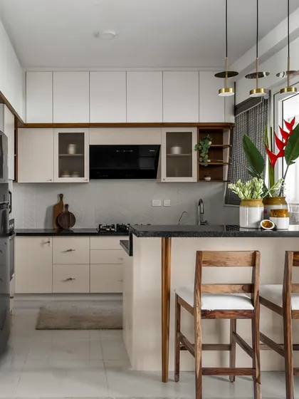 The kitchen in our 'Malhar' project uses a mellow monochrome palette with a light blush tone, broken by warm wooden hues. The space includes a breakfast counter for casual dining.
