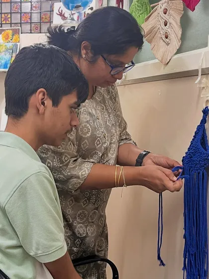 I believe in gentle, one-on-one guidance. Here, I'm helping a student with a macrame knot, ensuring he feels supported and confident as he learns this new skill. This adaptive instruction is at the heart of our special needs art program.