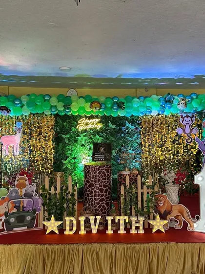 A full-stage jungle theme with a green and yellow shimmer backdrop. The setup is packed with details like lion and elephant cutouts, a 'BABY' block, and a large marquee number '1'.