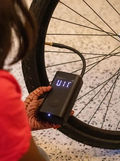 A child uses a portable electric pump to inflate a bicycle tire. We cover all aspects of bike maintenance, including using modern tools to make the job easier.