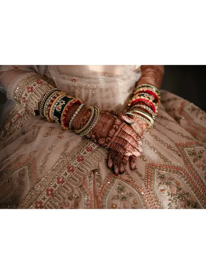 A close-up on the bride's hands, showcasing her intricate bangles and mehendi, a beautiful detail of her bridal attire.