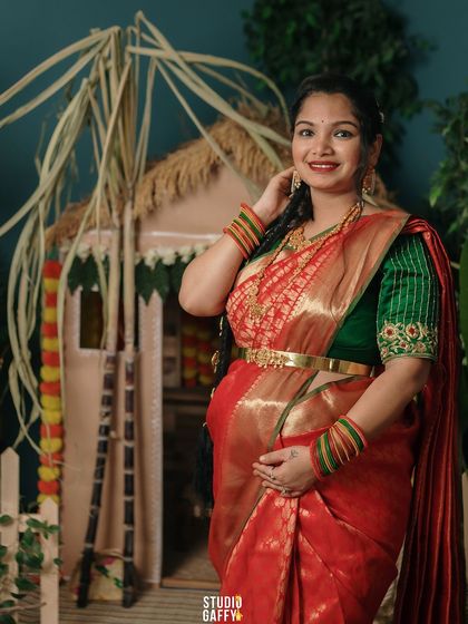 The mother-to-be shines in a traditional red and green saree, her hands gently cradling her bump.