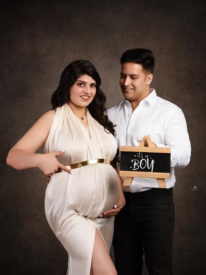 A fun and happy gender reveal moment. The mom-to-be points to her bump as her partner holds the 'It's a Boy' sign, capturing their shared excitement.