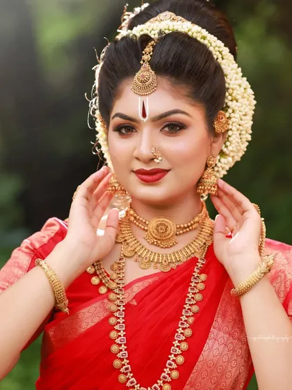 A bright and joyful portrait. The bride's smile is infectious, and the natural outdoor lighting brings out the rich colors of her red saree and gold jewelry.