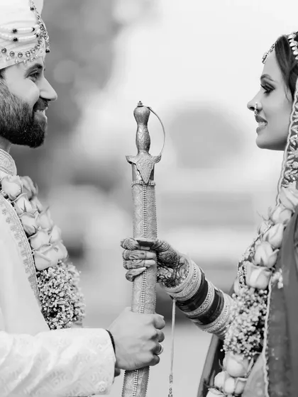 A black and white portrait capturing a traditional moment where the bride presents a sword to the groom.